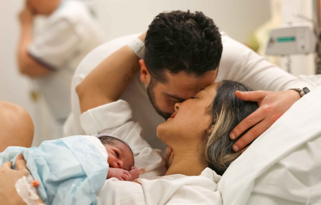 Partner kissing mother while newborn rests on her chest after birth in The Hague.