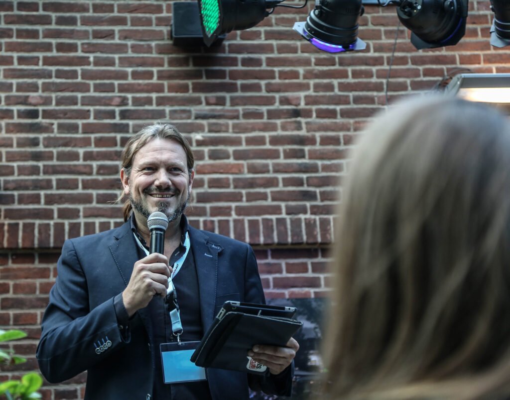 Event host smiling while speaking into a microphone during a corporate gathering in The Hague.