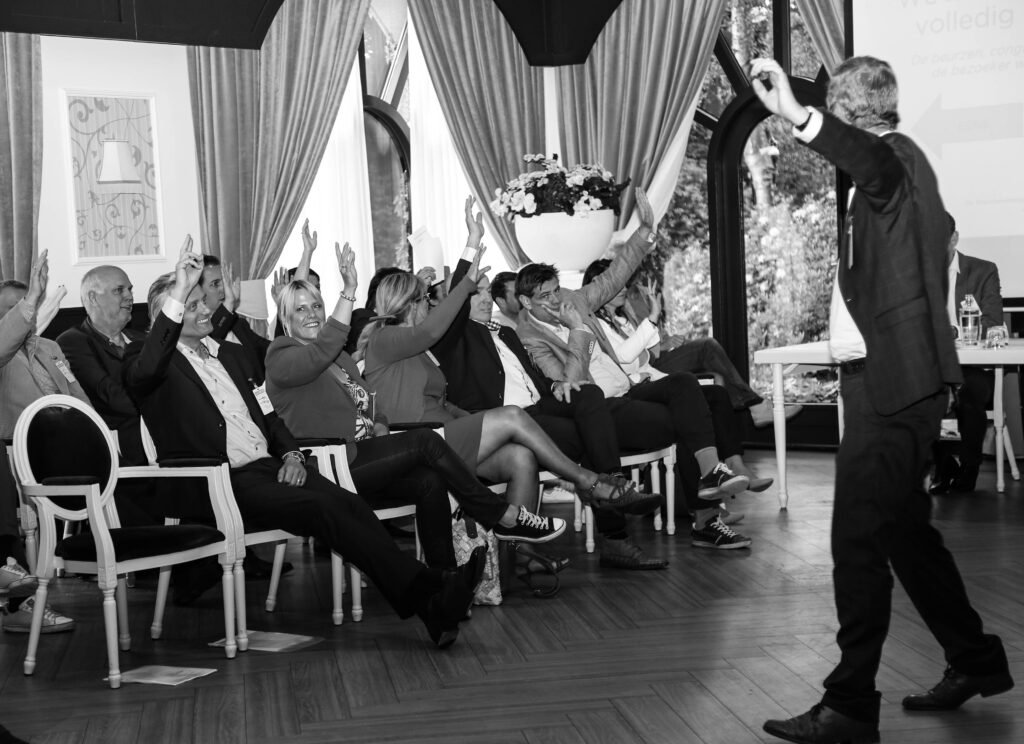 Business audience raising hands during an interactive session at a corporate event in The Hague.