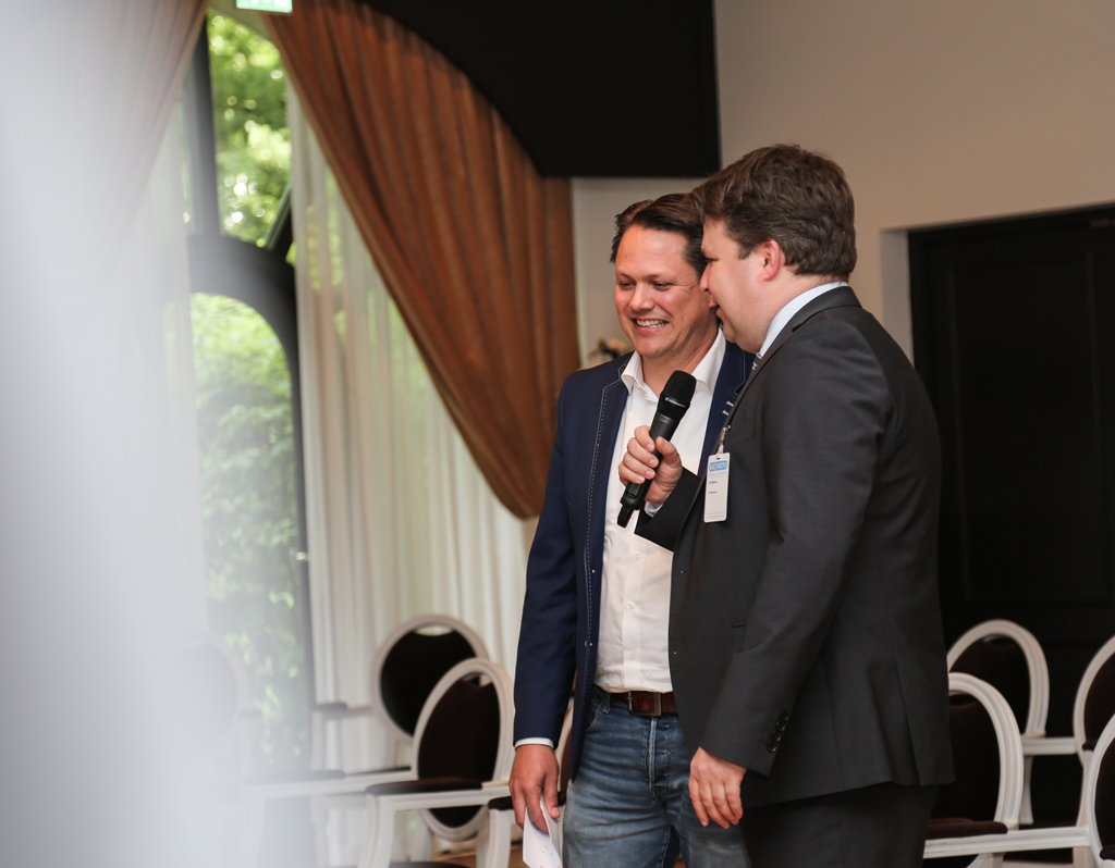 Two speakers sharing a microphone during a corporate event in The Hague.