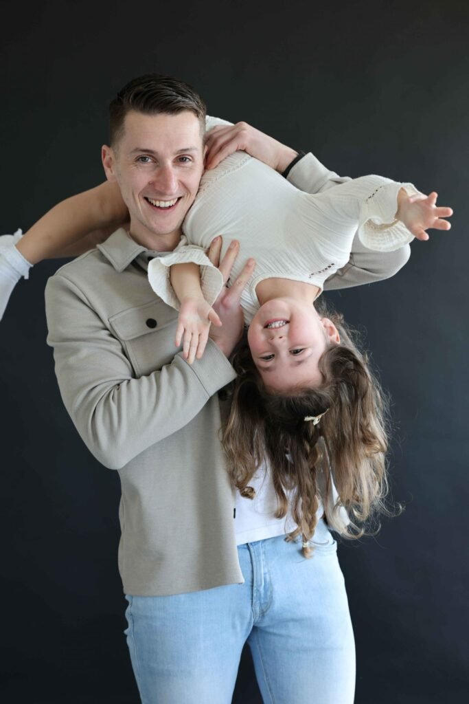 Father holding his laughing daughter upside down during a playful family portrait.