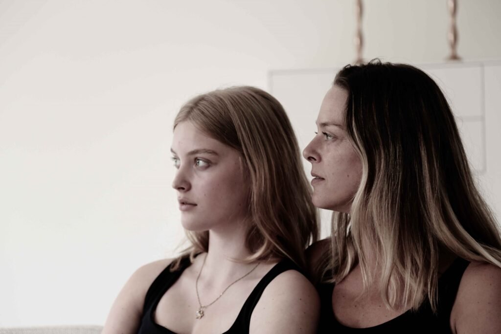 Mother and teenage daughter photographed in soft natural tones, looking into the distance.