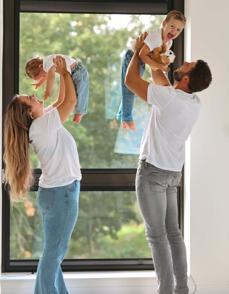 Parents lifting their two young children playfully during a natural-light family photoshoot.