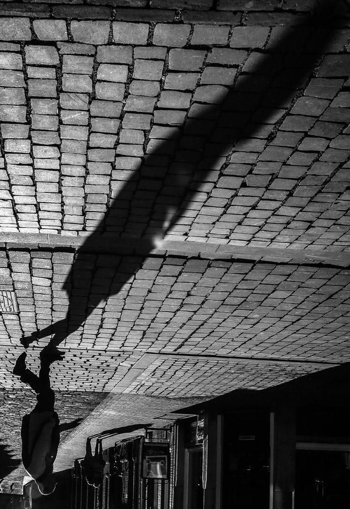 Black and white street scene with long shadows on cobblestones