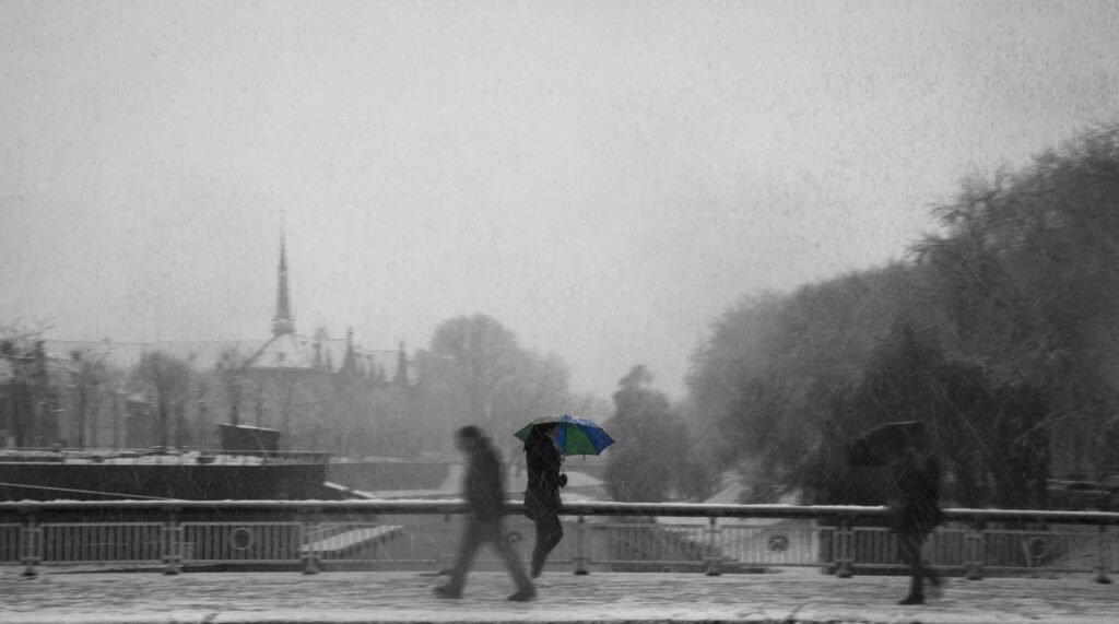 People walking on a bridge in heavy snow with one colourful umbrella