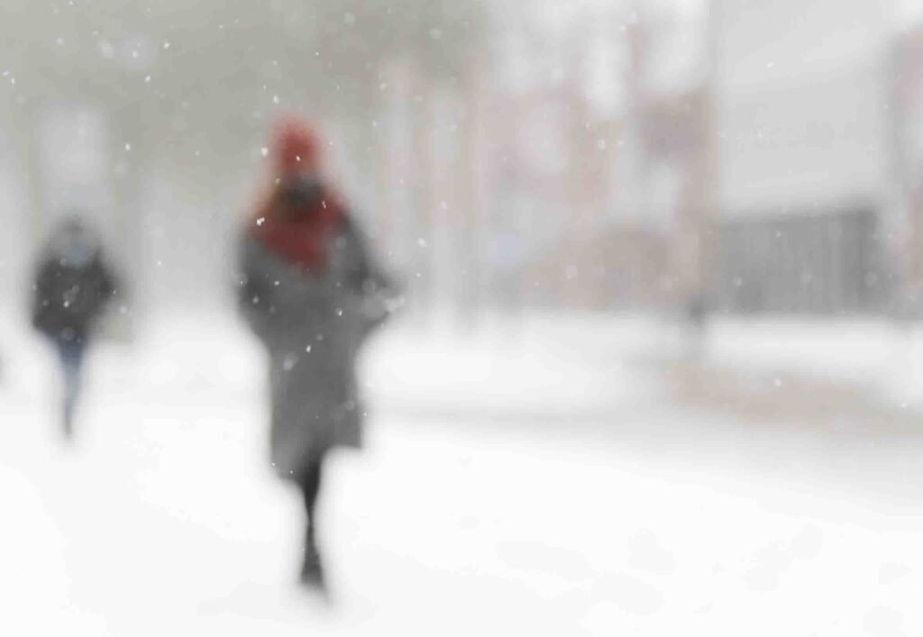 Soft-focus snowy street scene with silhouettes of people