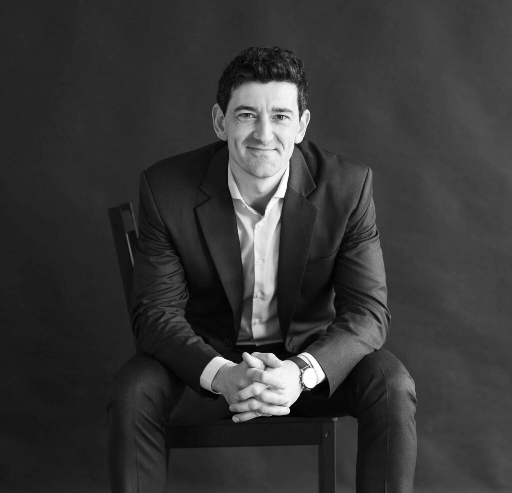 Professional male business portrait in a suit, seated and smiling in a dark studio – The Hague.
