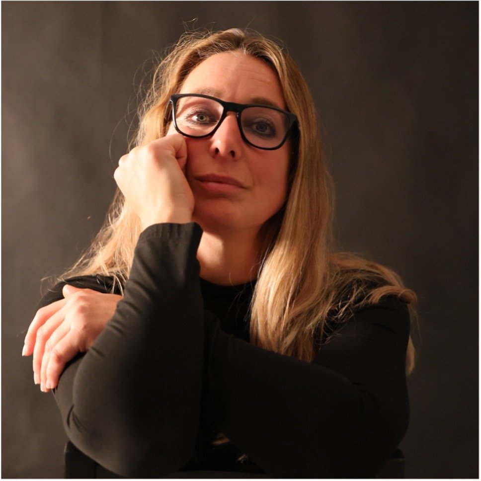 Woman with glasses in a soft studio light, leaning on her hand — LinkedIn portrait in The Hague.