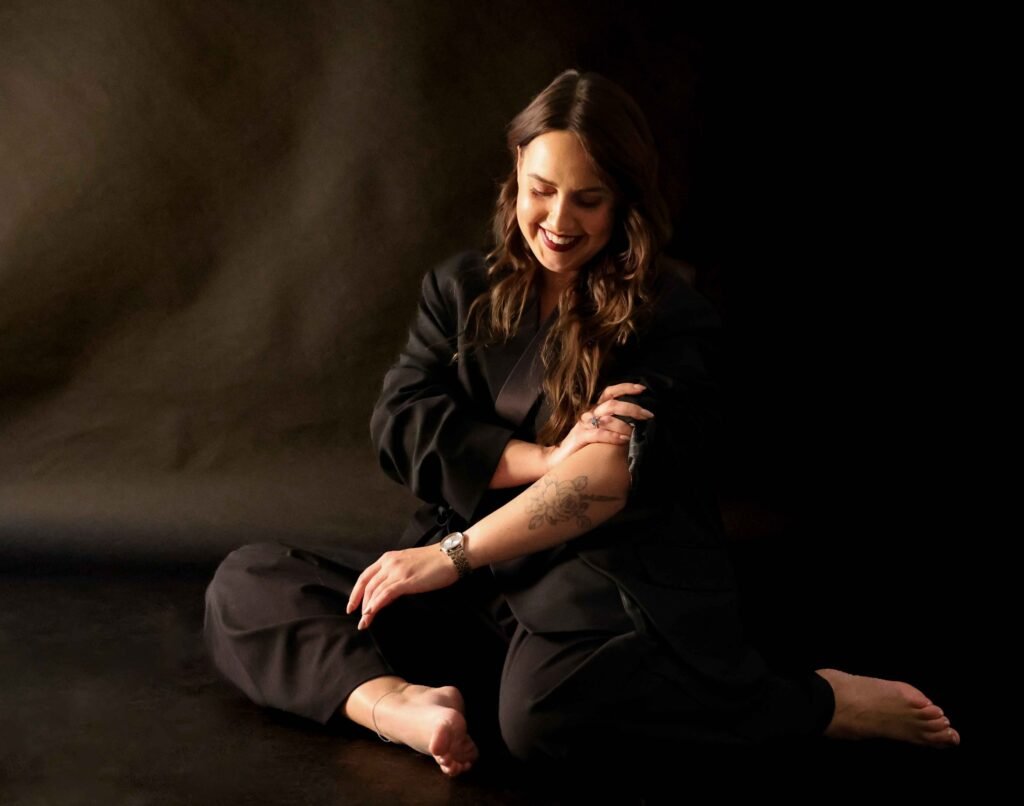 Professional woman sitting on the floor in a dark studio, smiling with arms folded — LinkedIn portrait in The Hague.