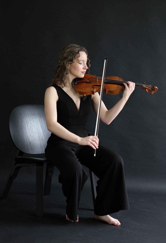 Professional violinist seated with violin, photographed in studio — creative LinkedIn portrait in The Hague.