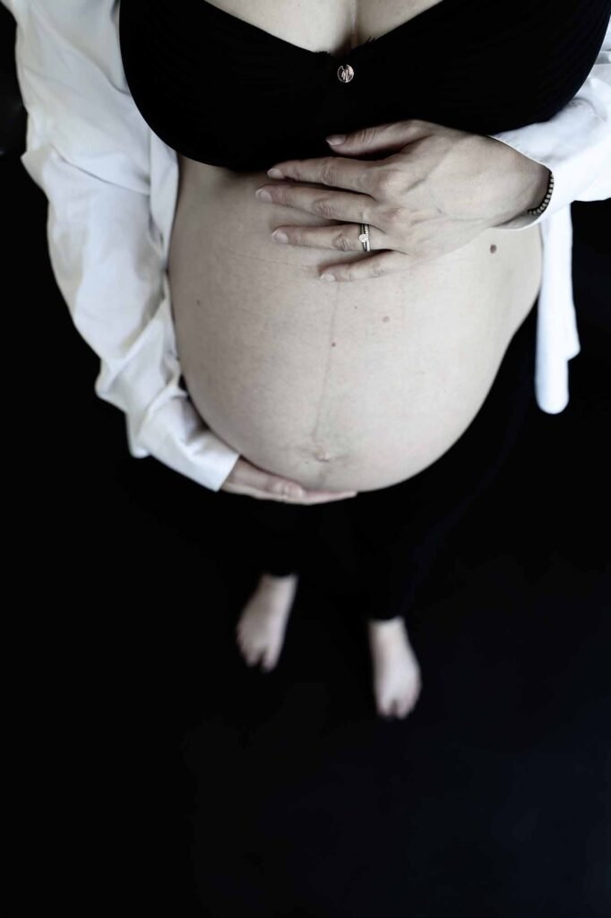 Close-up of a pregnant belly with hands gently placed on top during a minimalist studio maternity shoot.