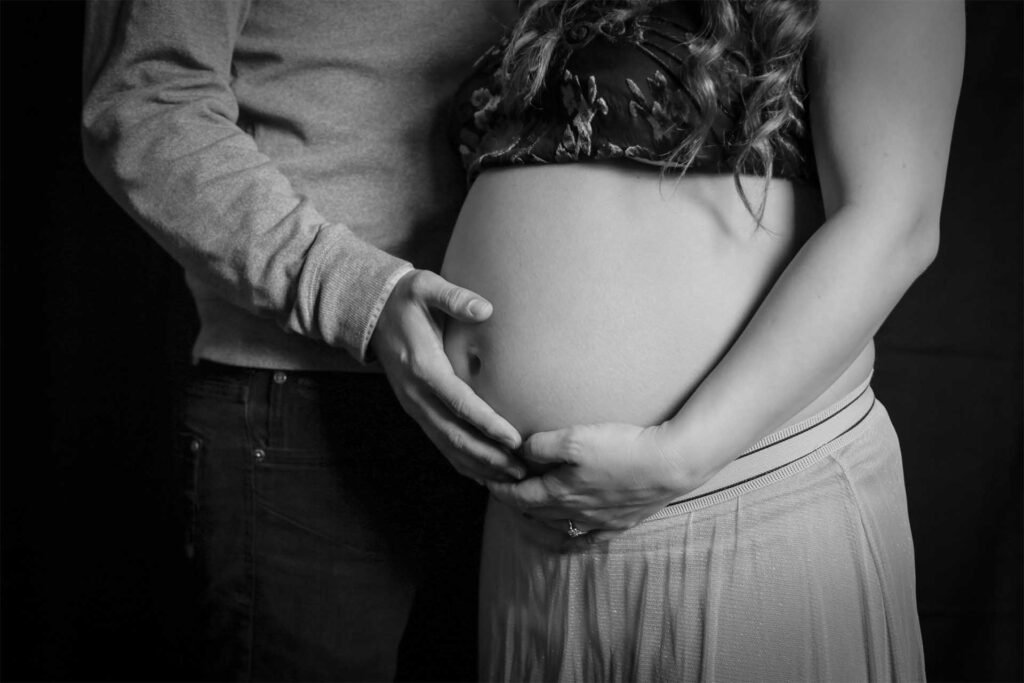 Black and white maternity photo of a couple holding the baby bump together in The Hague.