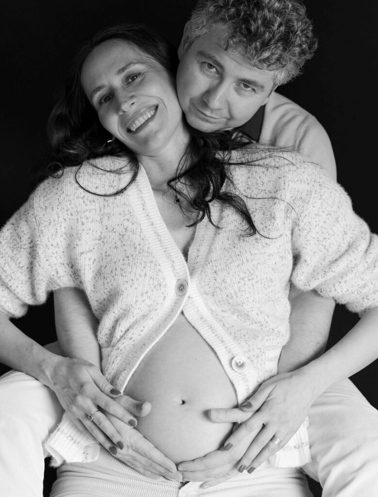 Smiling expectant couple embracing during a studio maternity photoshoot.