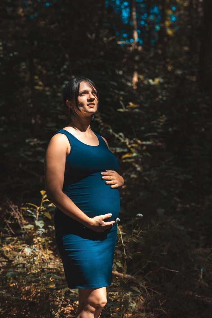 Outdoor maternity portrait in forest light with expecting mother holding her belly in The Hague.