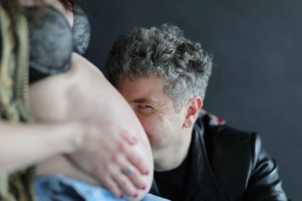 Partner smiling while leaning close to a pregnant belly during a maternity photoshoot in The Hague.