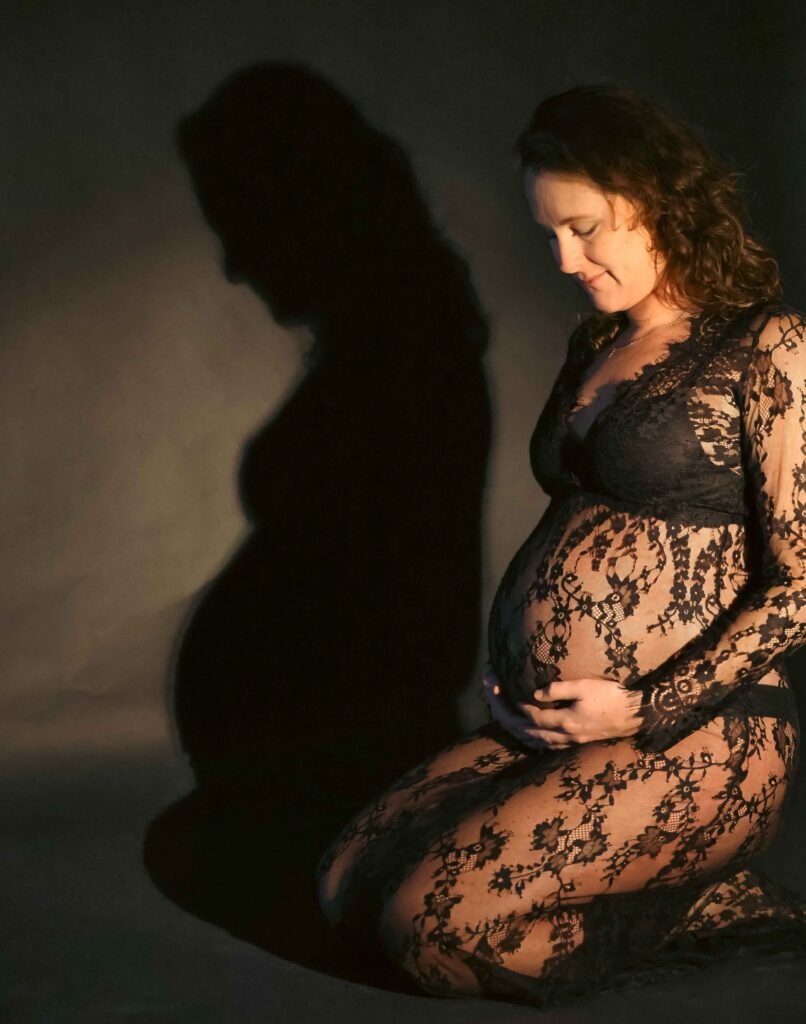 Pregnant woman kneeling in lace dress with dramatic shadow on the wall in a studio in The Hague.