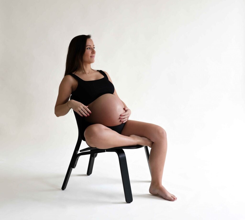 Pregnant woman seated on a chair in a minimalist white studio in The Hague.