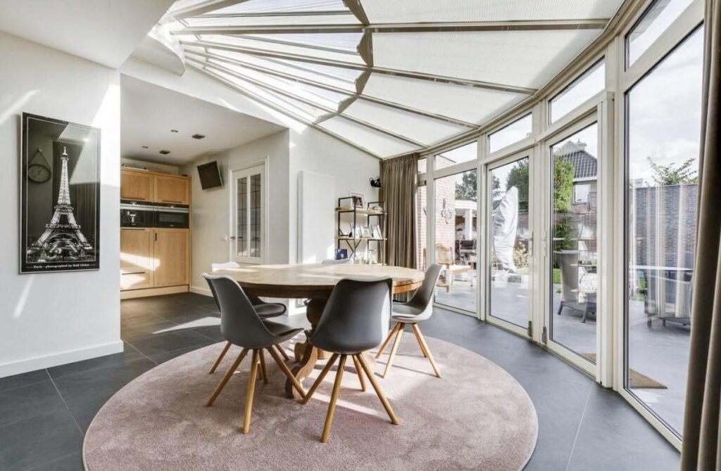Glass conservatory dining room with round table and garden access in The Hague