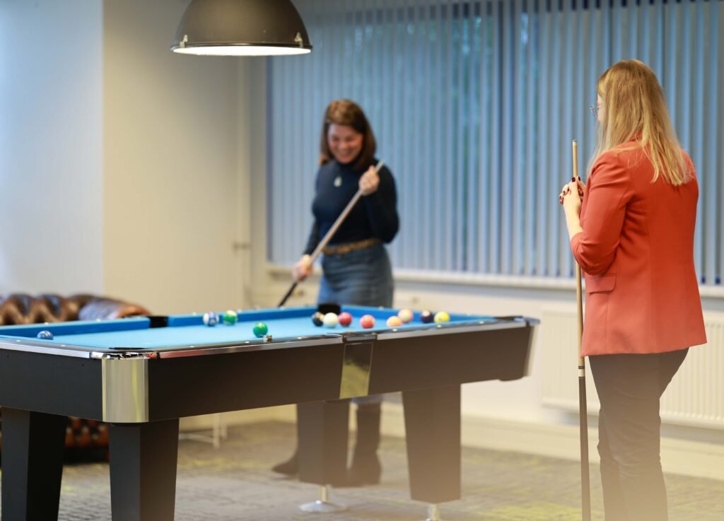 Two colleagues playing pool together in an office recreation area in The Hague